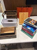 Photo showing all items arranged on a white table including baskets, plastic container, orange bag, wooden book stand, stack of books.