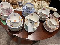 13 teacups and saucers showing assortment of floral and decorative patterns on a wooden table