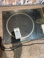 Kenwood turntable with closed plastic dust cover showing scratches and power cord on carpet floor
