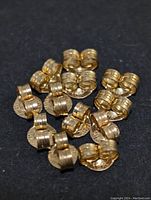 Multiple 10K gold earring backs grouped on a black surface, showing smooth, cylindrical shapes with ridged sections.