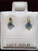 Pair of earrings with square cut blue topaz and small round diamonds in 10K gold on white textured display card.