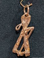 Close up front view of 10K gold pendant showing textured triple golf club design and gold loop.