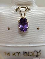 Front view of the 14K gold pendant with oval amethyst gemstone displayed on a white jewelry holder showing 14 KT gold marking.