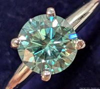 Close-up of round moissanite gemstone set in 10K gold ring with four prongs, showing sparkle and light reflection.