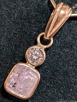 Close-up of pendant front, showing pink cushion cut diamond and round white diamond.