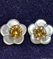 Front view of the two flower-shaped earrings with brown diamonds in the center and white mother of pearl petals.