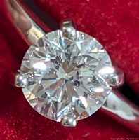 Close-up of round brilliant-cut diamond in six-prong 14K white gold setting against red background.
