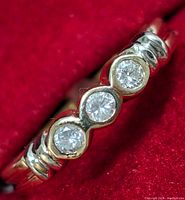 Close-up top view of three bezel-set round diamonds on yellow gold band against red background