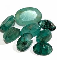 Photo showing 9 faceted emerald gemstones of varying green shades and sizes.