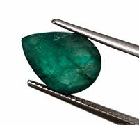 Close-up of genuine pear-shaped emerald gemstone held by tweezers showing color, shape and inclusions