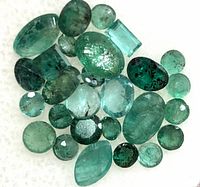 Top view close-up of a variety of emerald gemstones in different cuts and sizes laid out on white background