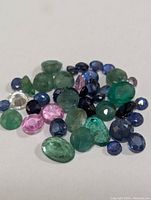Loose collection of green, blue, and pink faceted gemstones on white background