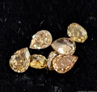 Close-up of seven small fancy color diamonds on a black background showing their pear and oval cuts and yellow to brown hues.