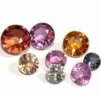 Eight loose round cut sapphires in multiple colors displayed on a white background, showing various hues and clarity.
