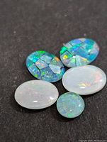 Five polished opalite and mosaic opal cabochon gemstones on a black background.