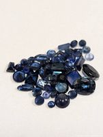 Various loose blue sapphire gemstones in different shapes and sizes spread on white background.