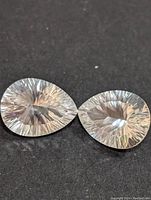 Close view of two pear-shaped white topaz faceted gemstones showing top view on dark background