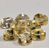 Seven oval-cut yellow sapphire gemstones on a white background, showing their color and cut.
