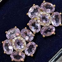 Close-up of one earring showing faceted oval amethyst stones arranged in floral cluster with yellow gold prongs.