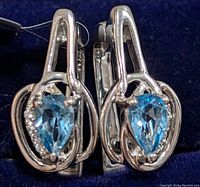 Pair of silver earrings with pear-shaped blue topaz stones in open teardrop silver settings, shown from front.