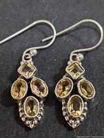 Front view of the pair of silver earrings with yellow-orange citrine stones arranged in square and oval shapes.