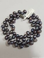 Full view of coiled necklace showcasing peacock-colored oval pearls and the clasp with diamond details.