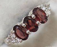 Close-up front view of silver ring with three oval garnet stones and cubic zirconia clusters on each side.
