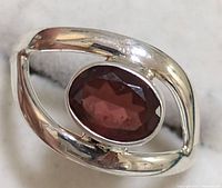 Close-up front view of silver ring with large oval garnet stone, showing stone faceting and silver band design.