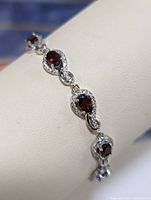 Close-up of sterling silver bracelet showing the multiple oval garnet gemstones surrounded by clear cubic zirconia stones linked in an infinity loop design.
