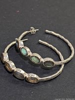 Pair of large silver hoop earrings with four bezel-set oval labradorite stones on each, displayed on black background.