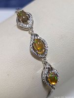 Close-up of three oval orange opal stones set in silver surrounded by cubic zirconia stones on bracelet