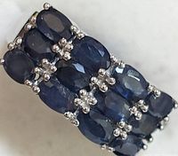 Close-up image showing the front view of the silver ring with three rows of oval-cut blue sapphires held in prong settings.