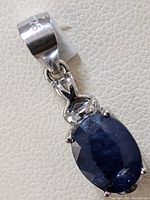Close-up image of silver pendant featuring oval faceted dark blue sapphire with silver bail stamped 925.