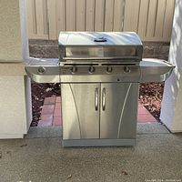 Front view of stainless steel Char-Broil grill showing four control knobs and double door cabinet under the grill surface.