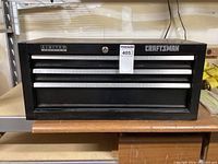 Front view of black Craftsman limited edition tool chest showing three drawers and lock with keyhole, silver handles, placed on a wooden surface.