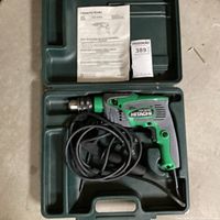 Hitachi Koki FDV 16VB2 drill placed inside molded plastic carrying case along with the detachable handle and power cord coiled.