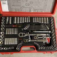 Open red plastic case showing organized chrome sockets, ratchets, wrenches, extensions, and screwdriver handle inside with a foam insert.