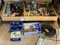 Full view of various irrigation fittings and connectors organized in two wooden trays atop a shelf, coiled irrigation tubing, boxed irrigation components, and a blue caddy with sprinkler tools.