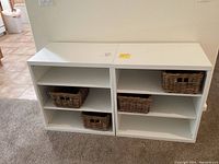 Two white melamine cabinets side-by-side, each with two shelves; two woven baskets placed on lower shelves in each cabinet.