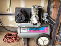 Full view of the Campbell Hausfeld Power-Pro air compressor on the floor with an orange extension cord coiled beside it.