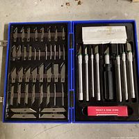 Open carrying case showing all interchangeable blades arranged on left side and knife handles along with accessories on right side.