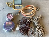 Photo showing yellow halogen work light with metal cage and stand, orange/white heavy-duty rope with metal hooks, beige natural fiber rope, black/orange braided rope, and coiled air hose in packaging.