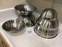 Photo showing six stainless steel mixing bowls stacked and displayed. Bowls are of different sizes, polished surface.