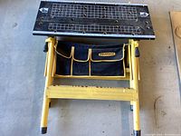 Top view of Workforce folding workbench showing metal grid surface and yellow legs with attached tool pouch.