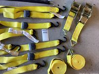 Six yellow ratchet straps with black ratchet mechanisms and metal hooks, plus two rolled yellow straps, laid flat on the floor.