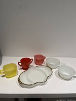 Assorted kitchenware including colorful cups and a white oval plate with gold dots.