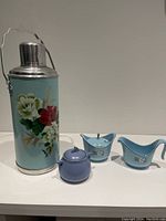 Photo of vintage metal thermos with floral design and blue ceramic cream and sugar set with solid blue sugar bowl.