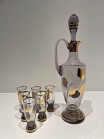 Photo showing decanter with stopper and six amethyst glasses decorated with gold leaf floral motifs and gold bands.