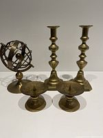 Photo showing two tall brass candle sticks, two short candle holders with spikes, and a decorative brass armillary globe.