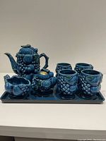 Full coffee/tea set arranged on serving tray showing teapot, sugar bowl, creamer and 4 cups all in blue ceramic with detailed fruit sculpting.